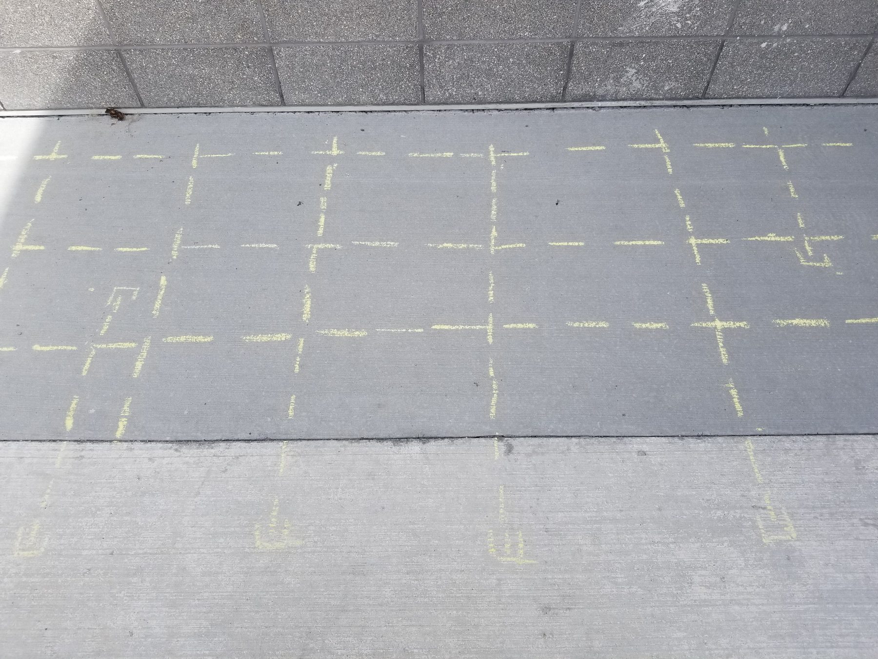 Yellow chalk grid marking dowel locations in a sidewalk slab