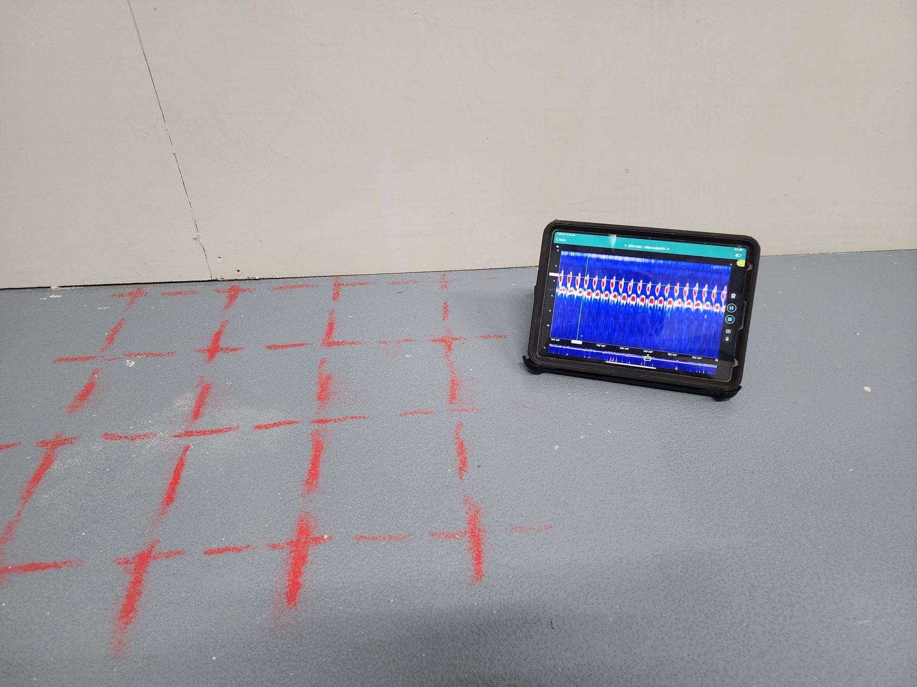 Rebar grid marked on a concrete slab beside a tablet showing the GPR radargram